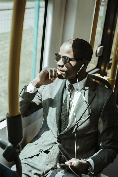 African american businessman wearing suit listening to music while taking train — Stock Photo