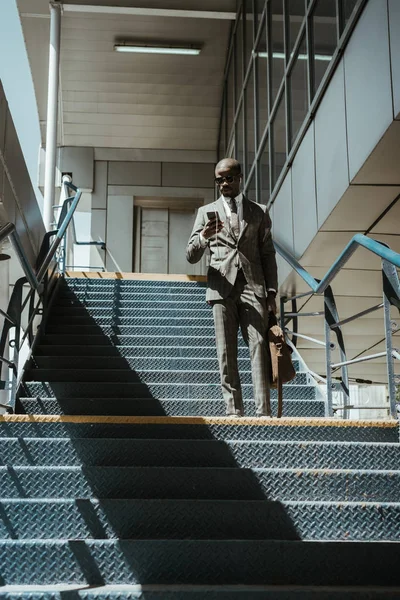 Jeune homme d'affaires afro-américain utilisant un smartphone tout en marchant dans les escaliers — Photo de stock