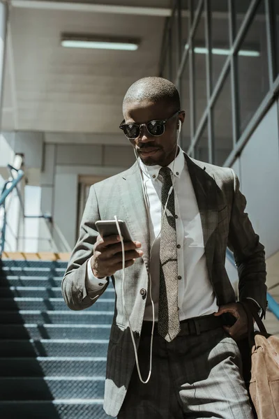 Stylish confident businessman using smartphone while walking on stairs — Stock Photo