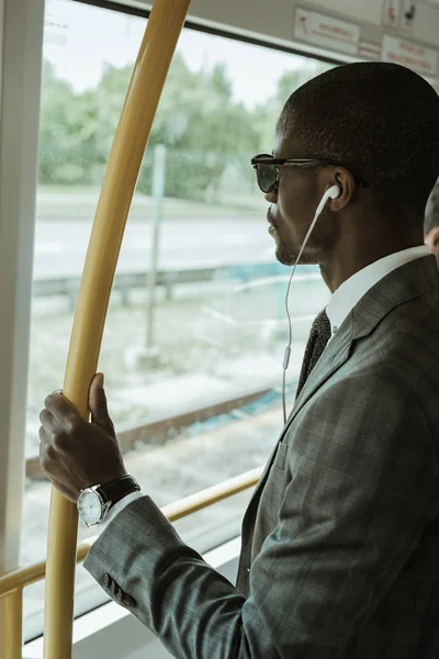 Empresario afroamericano confiado escuchando música mientras va a trabajar en tren - foto de stock