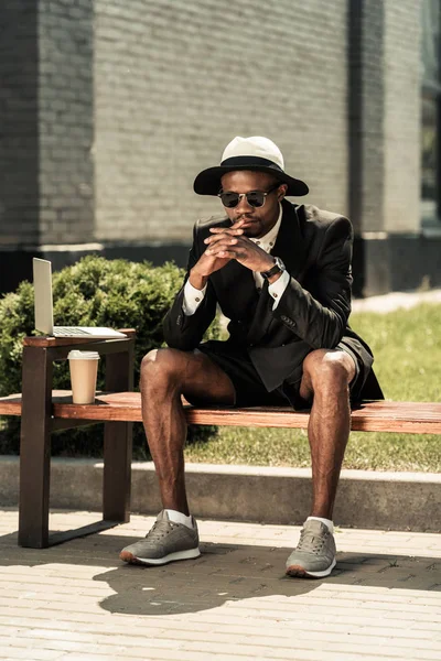 Schöner junger afrikanisch-amerikanischer Mann ruht sich auf Bank mit Laptop aus — Stockfoto
