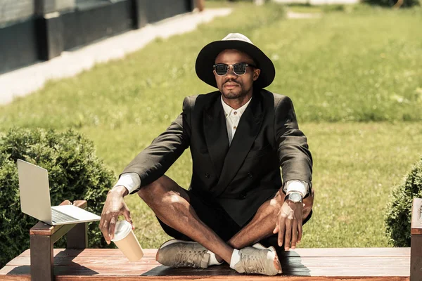 Bonito jovem afro-americano sentado no banco por laptop — Fotografia de Stock