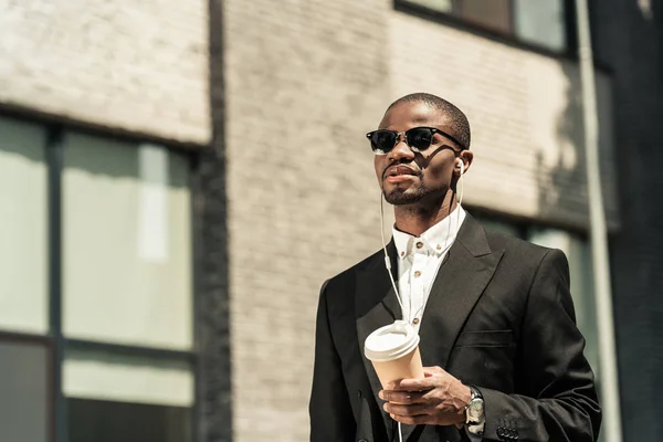 Homem elegante vestindo terno ouvir música e segurando xícara de café — Fotografia de Stock