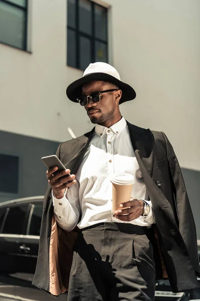 Bonito jovem empresário afro-americano ouvindo música e segurando xícara de café — Fotografia de Stock