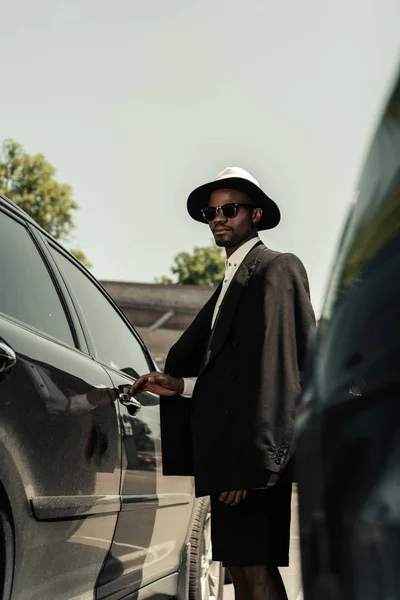 Homem americano africano na moda vestindo chapéu fedora abrindo porta do carro — Fotografia de Stock