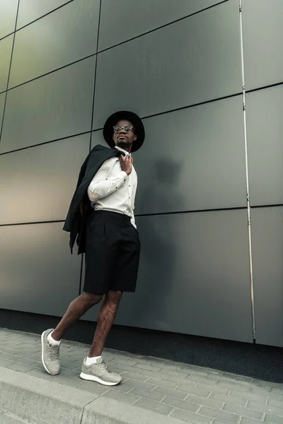 El hombre afroamericano de moda que usa sombrero de sombrero de sombrero y lleva su chaqueta - foto de stock