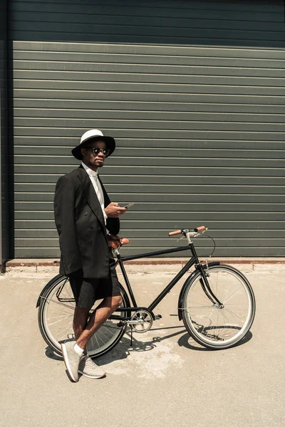 Стильний чоловік у білій сорочці та піджаку, використовуючи смартфон, тримаючи свій велосипед — стокове фото