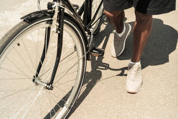 Vista recortada del hombre afroamericano de pie junto a su bicicleta - foto de stock