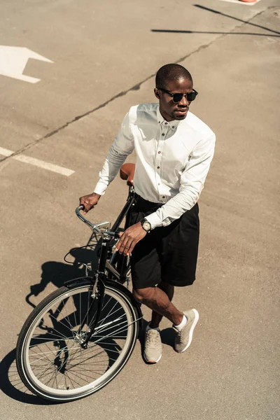 Guapo joven afroamericano hombre inclinado su bicicleta en la calle - foto de stock