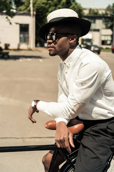 Guapo joven afroamericano hombre inclinado su bicicleta en la calle - foto de stock