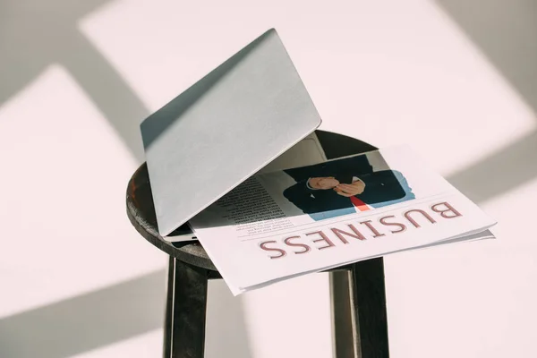 Close-up view of laptop with business newspaper on wooden stool on grey — Stock Photo