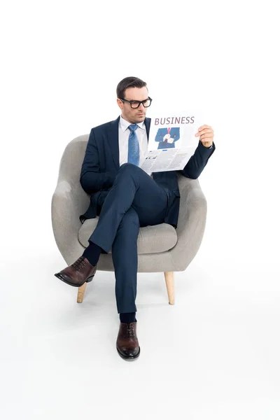 Vista completa de hombre de negocios serio en anteojos leyendo periódico mientras está sentado en sillón aislado en blanco - foto de stock