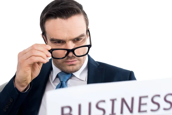 Close-up view of serious businessman reading newspaper and adjusting eyeglasses isolated on white — Stock Photo