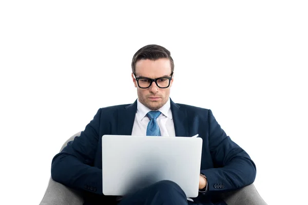Bello uomo d'affari in occhiali seduto in poltrona e utilizzando computer portatile isolato su bianco — Foto stock
