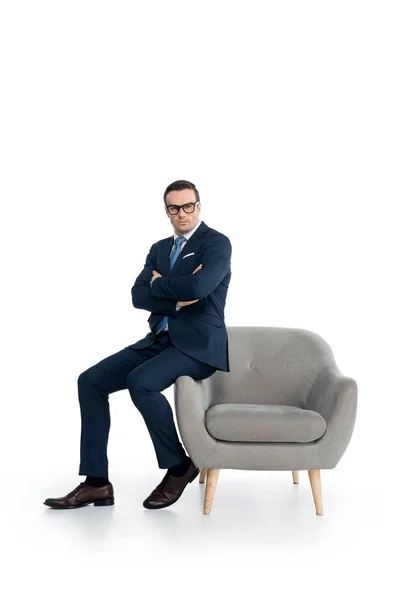 Full length view of confident businessman in eyeglasses sitting with crossed arms and looking at camera on white — Stock Photo