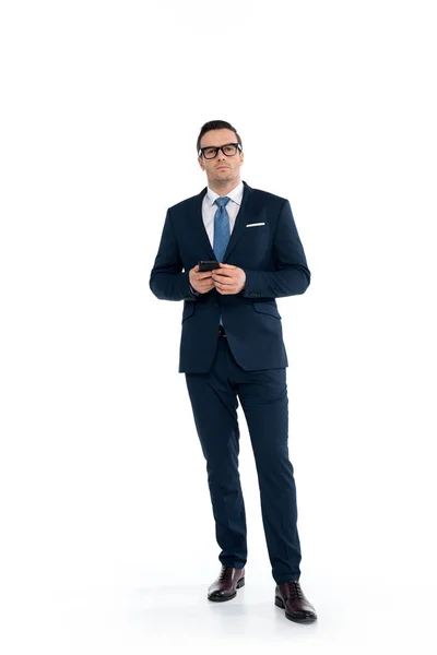 Full length view of confident buisnessman in eyeglasses holding smartphone and looking at camera isolated on white — Stock Photo