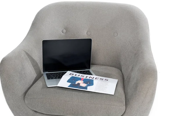 Laptop with blank screen and business newspaper on grey armchair — Stock Photo