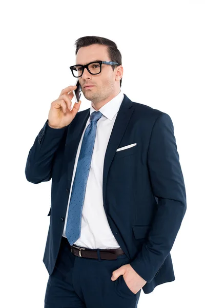 Guapo hombre de negocios en ropa formal hablando por teléfono inteligente y mirando hacia otro lado aislado en blanco - foto de stock