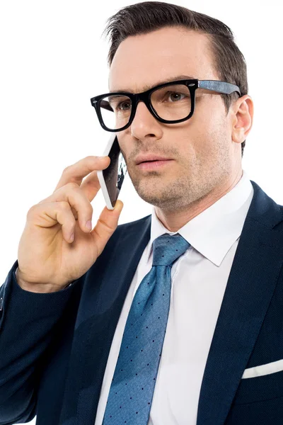 Homem de negócios bonito em óculos falando por smartphone e olhando para longe isolado no branco — Fotografia de Stock