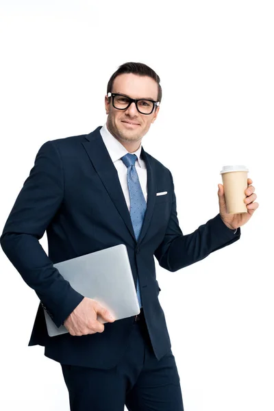 Handsome businessman holding laptop and paper cup and smiling at camera isolated on white — Stock Photo