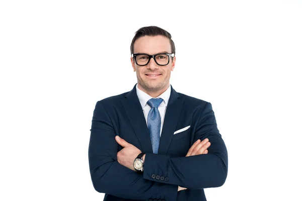 Uomo d'affari fiducioso in occhiali in piedi con le braccia incrociate e sorridente alla fotocamera isolata su bianco — Foto stock