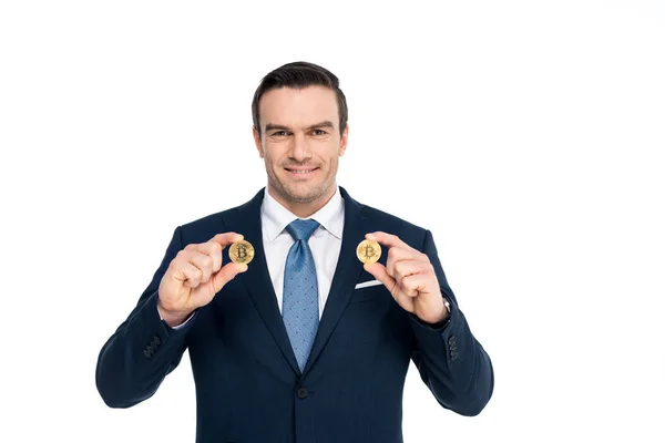 Guapo hombre de negocios de mediana edad sosteniendo bitcoins y sonriendo a la cámara aislado en blanco - foto de stock