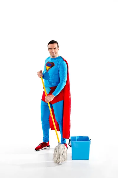 Handsome superman holdingholding mop and smiling at camera on white — Stock Photo