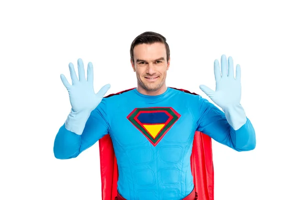 Handsome superhero showing hands in rubber gloves and smiling at camera isolated on white — Stock Photo