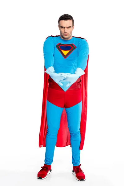 Vista completa del hombre serio en traje de superhéroe y guantes de goma estirando las manos y mirando a la cámara aislada en blanco - foto de stock