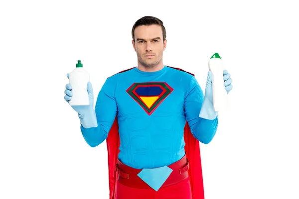 Serious man in superhero costume holding bottles with detergent and looking at camera isolated on white — Stock Photo