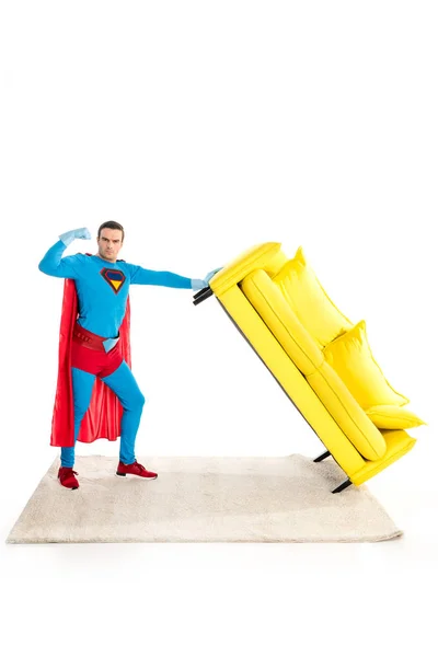 Superhéroe sosteniendo sofá y mostrando bíceps aislados en blanco - foto de stock
