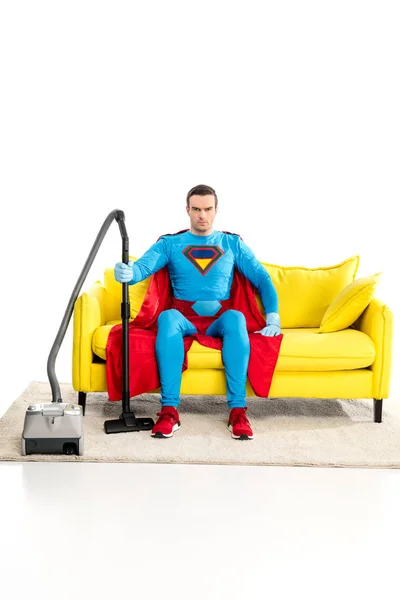 Superman mit Staubsauger sitzt auf der Couch und schaut in die Kamera auf weiß — Stockfoto