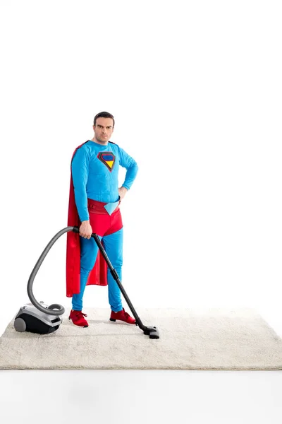 Confiance superman nettoyage tapis avec aspirateur et en regardant la caméra isolée sur blanc — Photo de stock