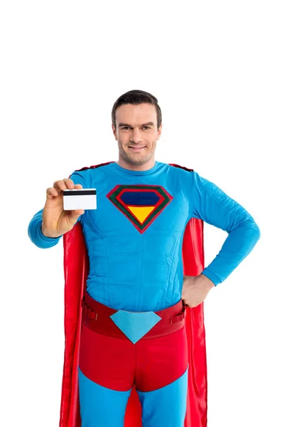 Schöner Mann im Superheldenkostüm hält Kreditkarte in der Hand und lächelt in die Kamera isoliert auf weiß — Stockfoto
