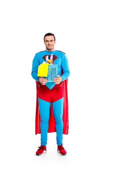 Handsome male superhero holding cleaning supplies and smiling at camera isolated on white — Stock Photo