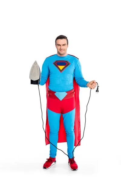 Улыбающийся мужчина супергерой держит железо и вилку изолированной на белом — стоковое фото