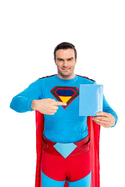 Guapo superman apuntando con el dedo a la caja en blanco con jabón en polvo y sonriendo a la cámara aislada en blanco - foto de stock