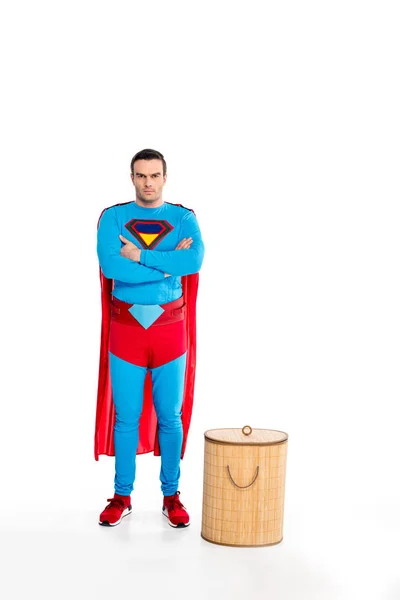 Schöner männlicher Superheld, der mit verschränkten Armen in der Nähe eines Wäschekorbs steht und isoliert auf weiß in die Kamera schaut — Stockfoto