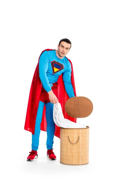 Handsome male superhero putting clothes in laundry basket and looking at camera isolated on white — Stock Photo