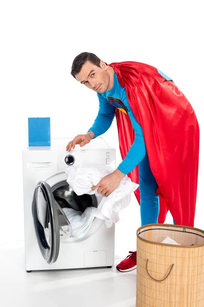 Супермен стирает одежду в стиральной машине и смотрит на камеру на белом — стоковое фото