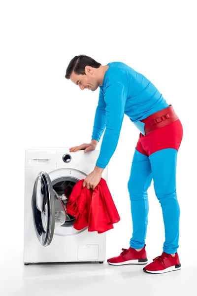 Souriant superman laver les vêtements dans la machine à laver sur blanc — Photo de stock