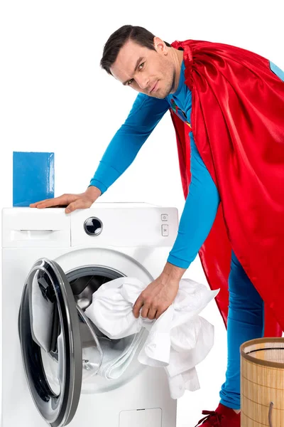 Superman washing clothes in washing machine and looking at camera on white — Stock Photo