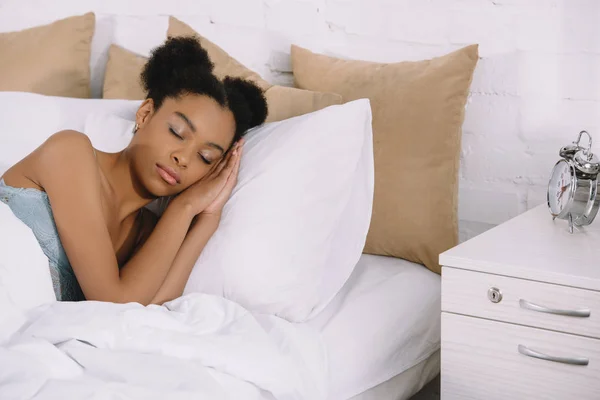 Beautiful african american girl sleeping on bed with alarm clock near — Stock Photo