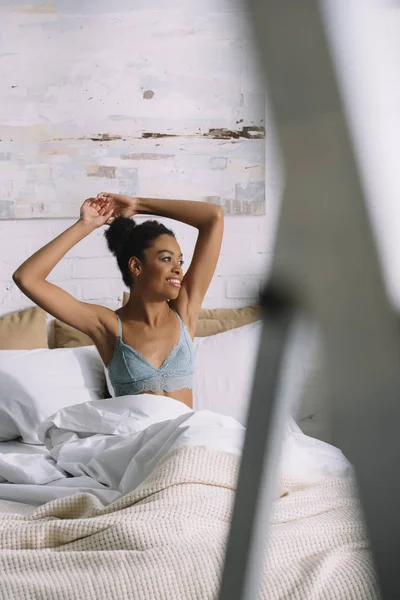 Sorridente donna afro-americana che si estende e si sveglia in camera da letto al mattino — Foto stock