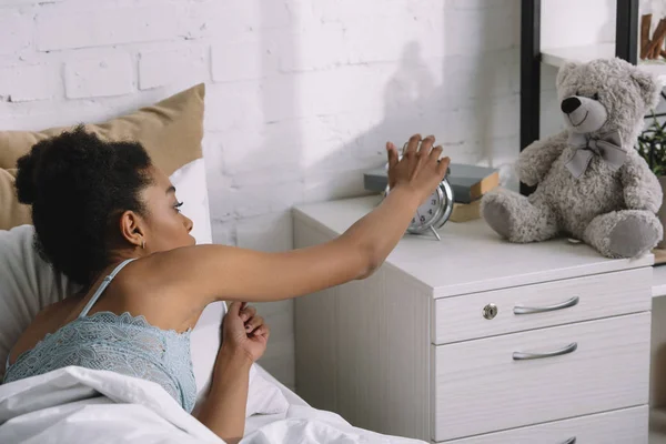 Африканская американская девушка просыпается и выключает будильник в спальне — стоковое фото