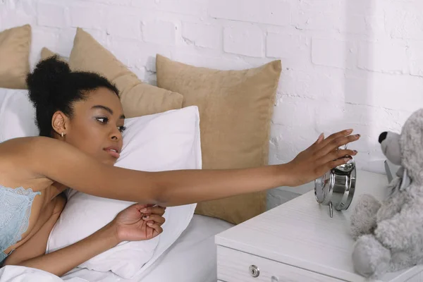 Bela menina americana africana acordar e desligar despertador na cama — Fotografia de Stock