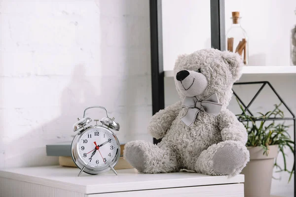 Alarm clock and grey teddy bear on nightstand — Stock Photo