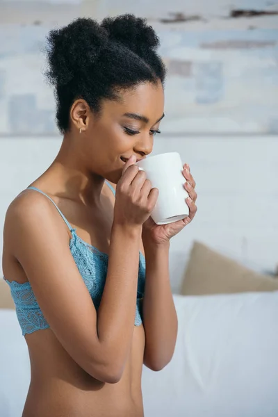 Happy african american girl drinking coffee in bedroom in morning — Stock Photo