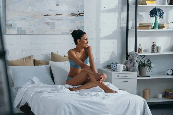 Cheerful african american girl in underwear sitting in bedroom in morning — Stock Photo