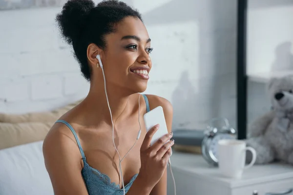 Atraente sorridente menina afro-americana ouvir música com fones de ouvido e smartphone — Fotografia de Stock